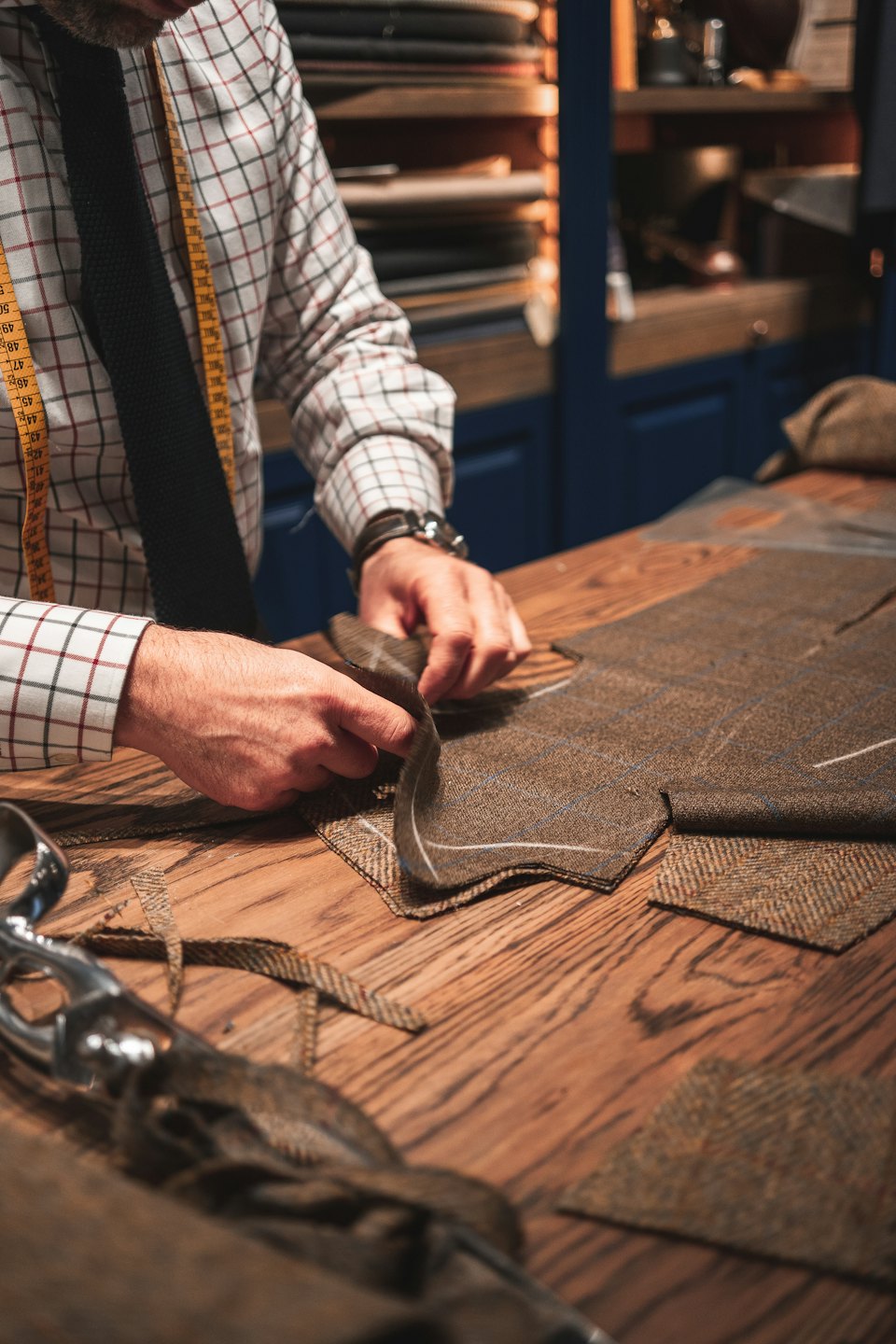 Mani di sarto lavorano tessuto di tweed su un banco da lavoro.